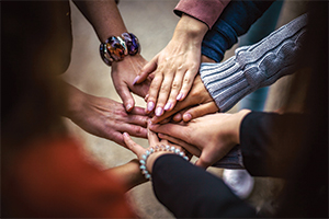 People standing in a circle with hands placed in the middle