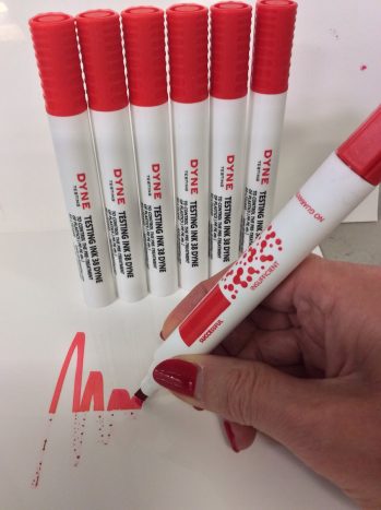 Dyne Testing Instant Dyne Pen 38 scribbling a red squiggle on a substrate to show treated versus untreated parts